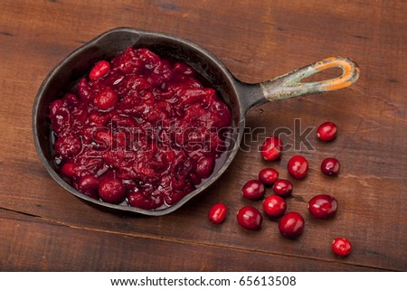 freshly fried cranberry sauce on a small iron pan and some fresh berries against old scratched wooden table top