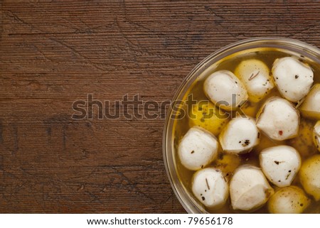 balls of mozzarella cheese marinated in oil with seasoning, glass bowl on weathered wood background