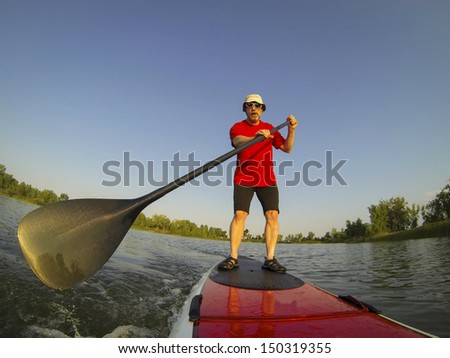 mature male paddler enjoying workout on stand up paddleboard (SUP), calm lake in Colorado, summer, distorted wide angle view