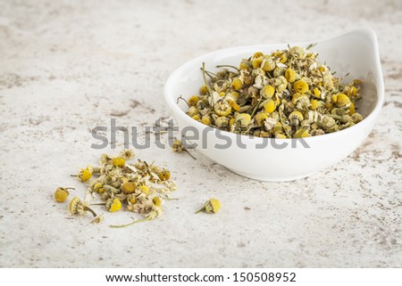 small ceramic bowl of  dried chamomile flowers against a ceramic tile background