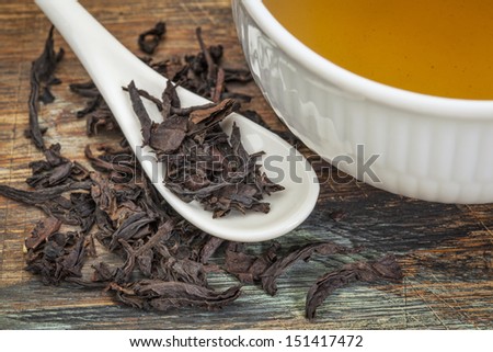 a cup of oolong black tea with loose leaf and teaspoon