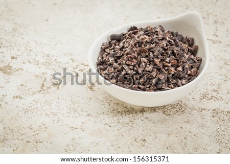 small ceramic bowl of  raw cacao nibs  against a ceramic tile background with a copy space