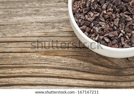 Raw Cacao Nibs In A Small Ceramic Bowl Against Grained Wooden Background