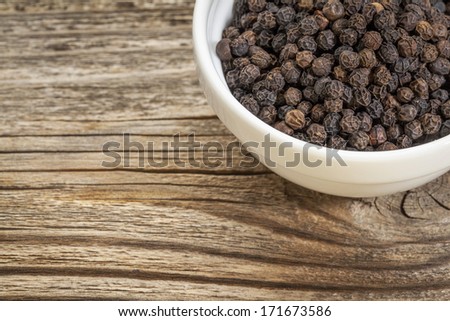 a bowl of black peppercorns against grained wood with copy space