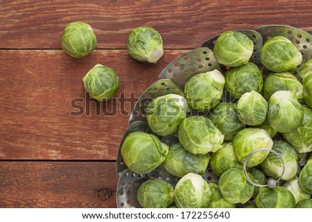 fresh Brussels sprouts in a metal steamer basket on red wooden rustic table