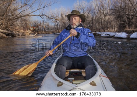 senior canoe paddler in a decked expedition canoe on the Cache la Poudre River, Fort Collins, Colorado, winter or early spring
