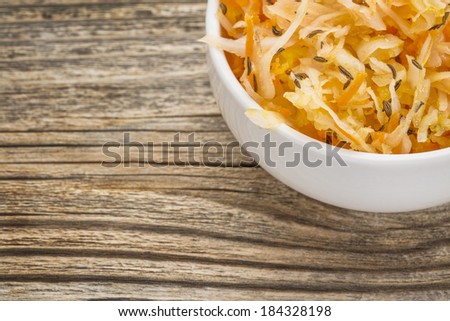 sauerkraut salad with carrot, caraway seeds and olive oil - a small bowl against grained wood