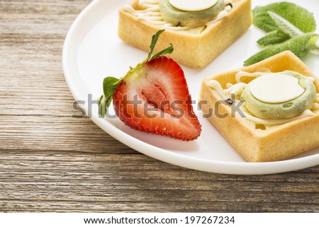 dessert - tarts with strawberry and fresh peppermint on white plate against grained weathered wood, top view