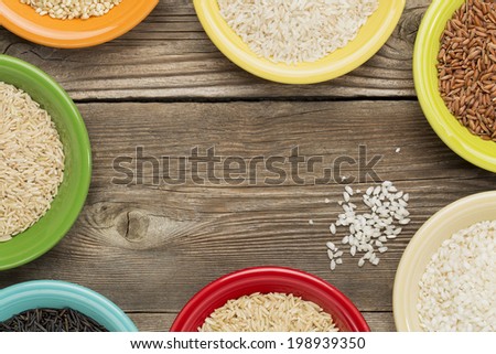a variety of rice grains on colorful ceramic bowls against a rustic wood, copy space