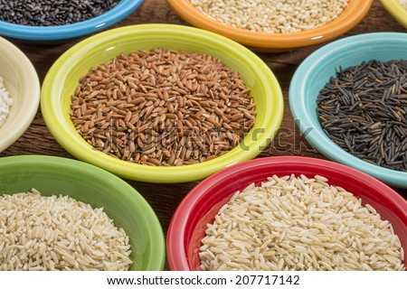 a variety of rice grains on colorful ceramic bowls against a grained wood