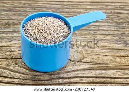 white chia seeds in measuring scoop against grained wooden surface