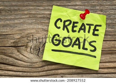 create goals reminder - handwriting on a green sticky note against grained and knotted wood board