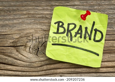 brand reminder - handwriting on a green sticky note against grained and knotted wood board
