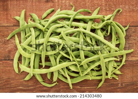 a pile of fresh green French beans on a rustic barn wood table, top view