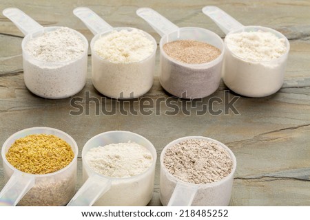 measuring scoops of gluten free flours - almond, coconut, teff, flaxseed meal, whole rice, brown rice, buckwheat, slate rock background