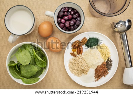 ingredients of healthy breakfast smoothie: almond milk, raw eggs, fresh spinach, frozen blueberries, whey protein, cacao, chia, pecans, maca root, spirulina, collagen protein, spices with a  blender