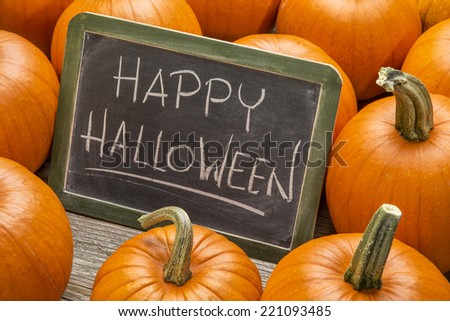 Happy Halloween - white chalk handwriting on a vintage slate blackboard surrounded by pumpkins