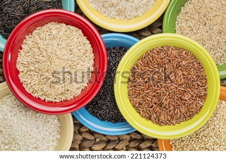 a variety of rice grains on colorful ceramic bowls against a woven water hyacinth mat, top view