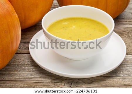 pumpkin cream soup - a bowl surrounded by pumpkins on a rustic wooden table