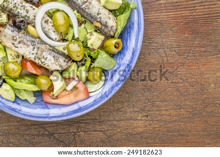 sardine salad (canned sardines, romaine lettuce, tomato, avocado, onion, olives) in bowl against grunge wood