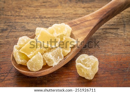 chunks of crystalised ginger  on a wooden spoon against grunge wood background