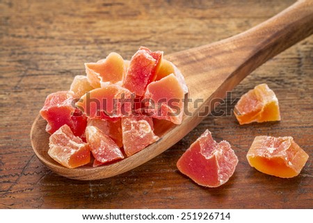 chunks of dried papaya fruit on a wooden spoon against grunge wood background