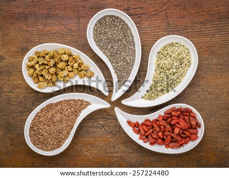 superfood samples  (mulberry, chia seeds, hemp seeds, goji berry, flax seed) in teardrop shaped bowls against grunge wood