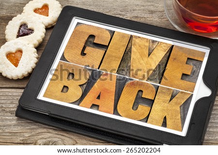 give back words text in letterpress wood type on a digital tablet with tea and heart cookies
