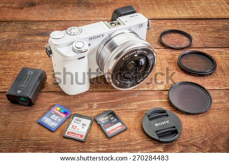 FORT COLLINS, CO, USA, April 17,  2015:  Sony A6000 mirrorless digital camera with a set of filters, memory cards, lens cap and battery on a grunge barn wood table