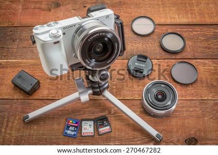 FORT COLLINS, CO, USA, April 17,  2015:  Sony A6000 mirrorless digital camera on a table tripod surrounded by a set of filters, memory cards, lens cap, battery and lens  on a grunge barn wood table.