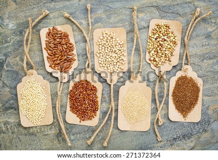 abstract of healthy, gluten free grains (quinoa, sorghum, brown rice, teff, buckwheat, amaranth, millet) - top view of paper price tags against a slate stone