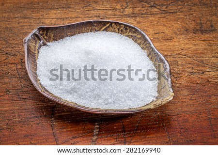 Epsom salts (Magnesium sulfate) in a leaf shaped ceramic bowl against rustic wood - relaxing bath concept