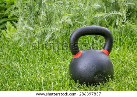 heavy iron competition kettlebell (62lb / 28 kg) on green grass in backyard - outdoor fitness concept