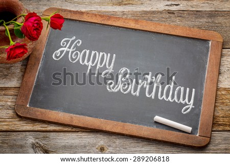 Happy Birthday greetings  - white chalk text on a vintage slate blackboard with red roses against rustic wood