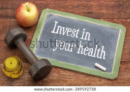 Invest in your health -  slate blackboard sign against weathered red painted barn wood with a dumbbell, apple and tape measure