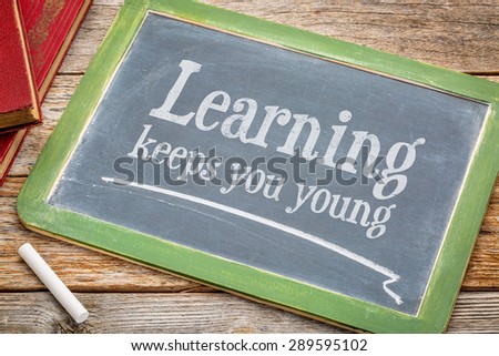 learning keeps you young - inspirational words with a white chalk on a blackboard with a stack of books against rustic wooden table