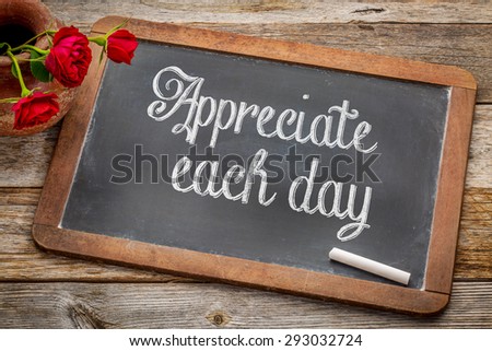 Appreciate each day  - white chalk text on a vintage slate blackboard with red roses against rustic wood