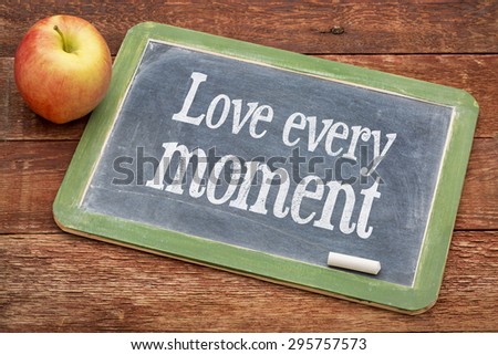Love every moment advice  - positive words on a slate blackboard against red barn wood