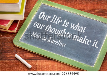 Our life is what our thoughts make it - inspirational word by Marcus Aurelius on a slate blackboard with a white chalk and a stack of books against rustic wooden table