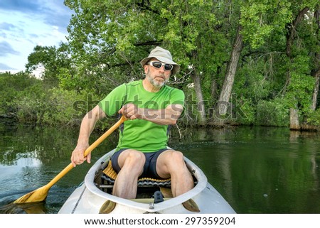 senior male paddler in a decked expedition canoe on a calm lake against background of trees