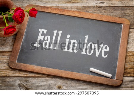 Fall in love advice  - white chalk text on a vintage slate blackboard with red roses against rustic wood