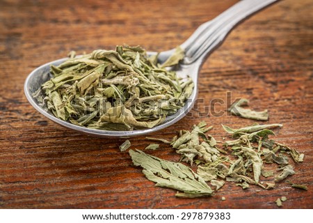 stevia dried leaves on a tablespoon against rustic woof - natural sweetener, sugar substitute
