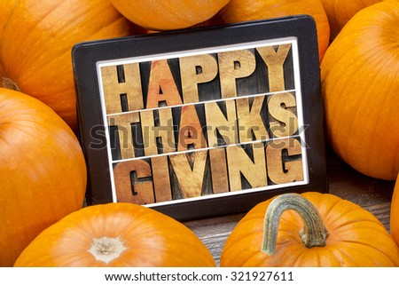 Happy Thanksgiving word abstract in letterpress wood type on a digital tablet surrounded by pumpkins