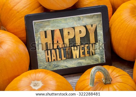 Happy Halloween - word abstract in letterpress wood type on a digital tablet surrounded by pumpkins