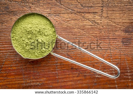 moringa leaf powder in a metal measuring scoop against rustic wood