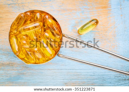 fish oil supplement capsules  in a metal measuring cup a painted grunge wood wood - top view