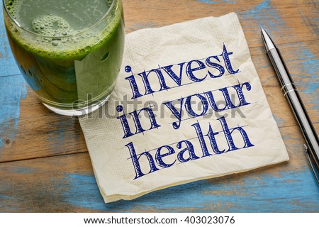 invest in your health advice or reminder - handwriting on a napkin with a glass of fresh, green, vegetable juice