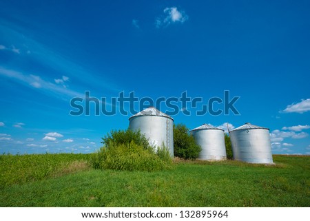 Three Grain Storage Containers on a Green Farm Field by a Clear Blue Sky