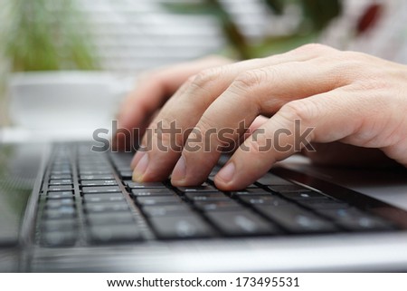 closeup of man typing on laptop in office with cup of coffee in blur