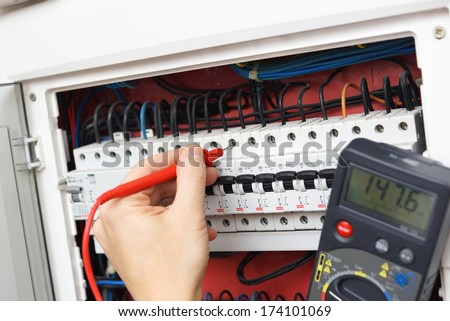 Hand of an electrician with multimeter probe at an electrical switchgear cabinet